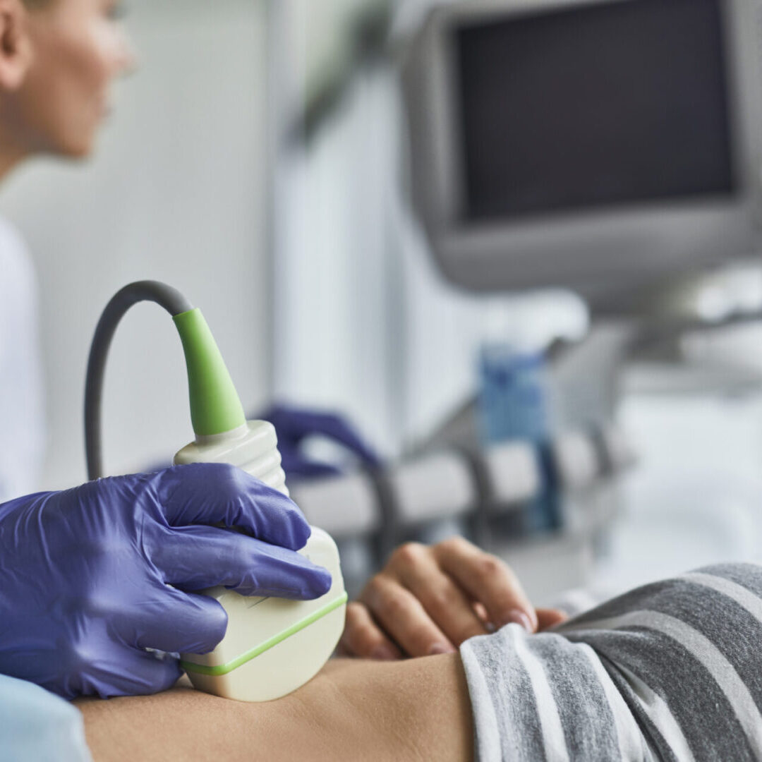 Doctora con guantes usando el transductor de la maquina de Ultrasonido mientras examina a una paciente.